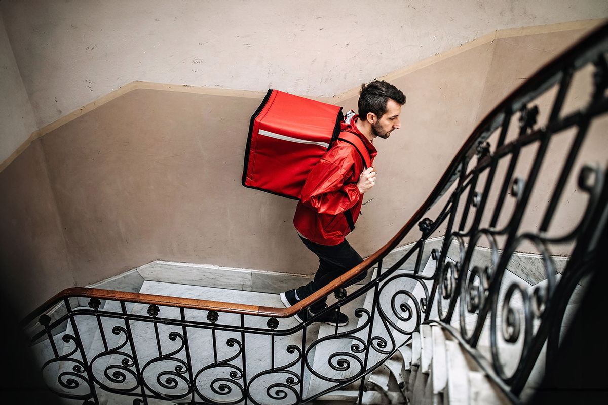 Delivery guy climbing up stairs in residential building, carrying container for food on his back (Getty Images/mixetto)