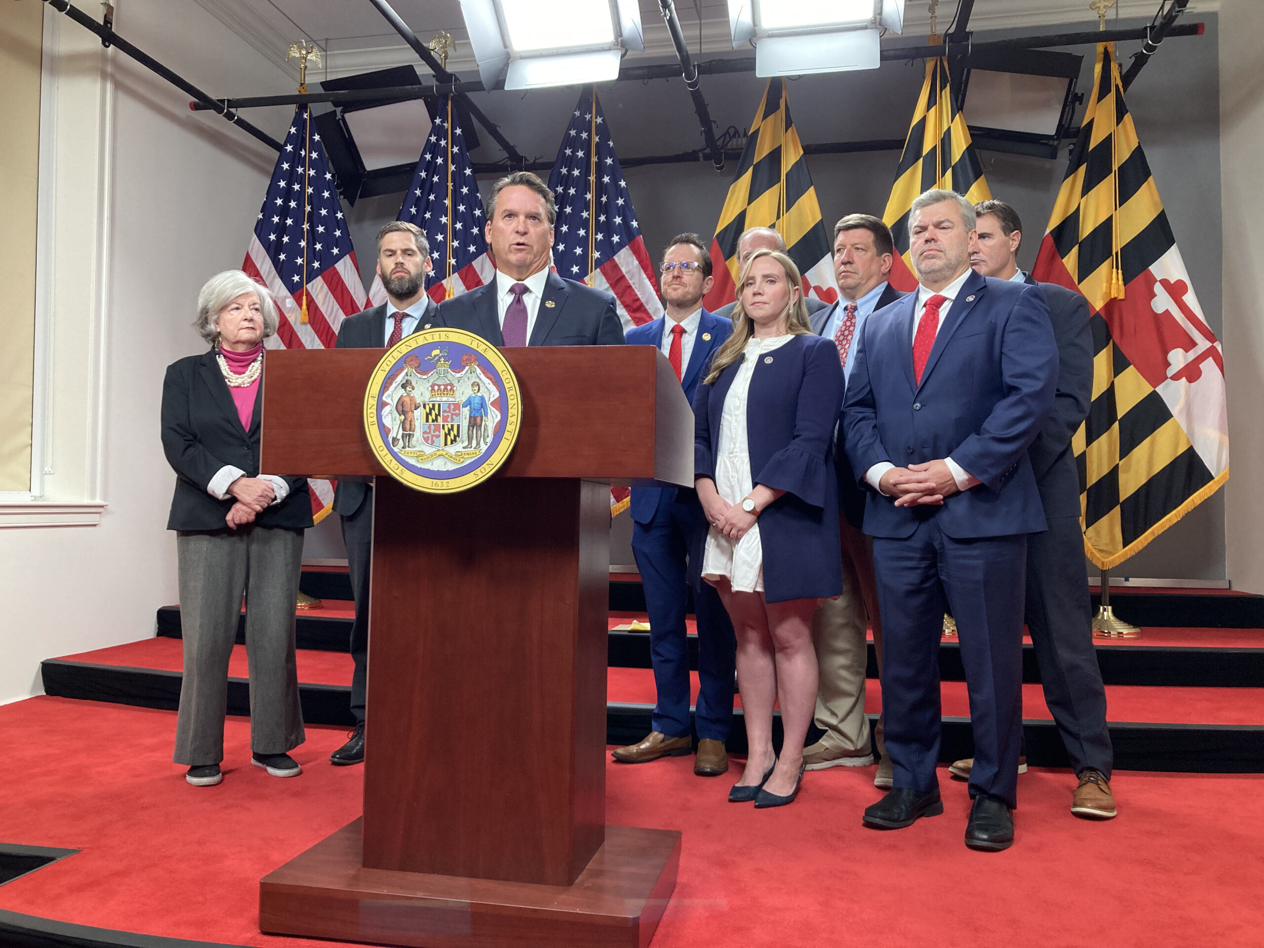 Members of the Maryland Joint Republican Caucus gather around a podium to announce their 2024 public safety agenda against a backdrop of Maryland and U.S. flags.