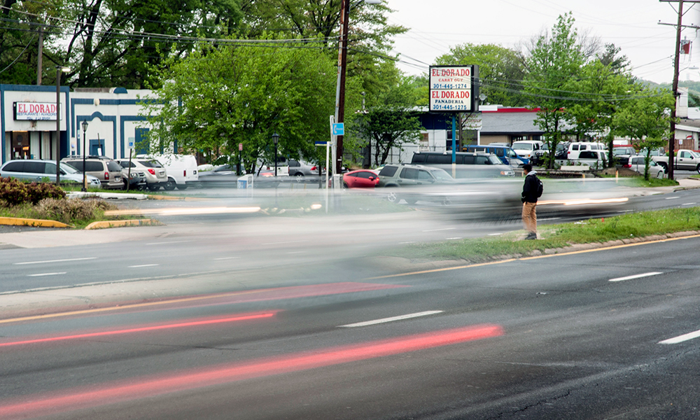 A man looks for a break in traffic to cross University Boulevard in Langley Park. In the past eight years, at least 138 pedestrians have been hit and eight have died on a two-mile stretch of the state highway that runs through the low-income, immigrant community outside Washington, D.C. (Capital News Service photo by Rebecca Rainey)