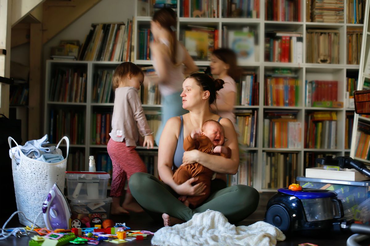 Tired, burnt-out mother with baby in her arms and out of focus children run around. (Getty Images/Natalia Lebedinskaia)