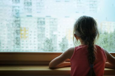 Little sad girl pensive looking through the rainy window.